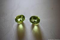 Two matching oval green peridot loose gemstones shown from top angle, highlighting faceted oval cut and vibrant color.