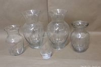 Five clear glass vases placed together on a beige surface, showing size and shape variations.