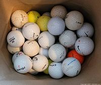 Top view photo showing a mix of over 50 used golf balls in various conditions inside a container.