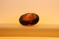 Close-up image of oval bi-colored tourmaline on light background, showing amber-orange hues with facets visible.