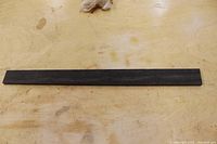 Top view of a long, narrow, dark Gabon Ebony wood piece on a light wooden surface.