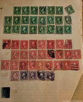 Close-up of multiple green and red U.S. postage stamps on lined paper, all used with cancellation marks.