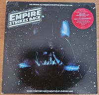 Front cover of the vinyl soundtrack album showing the Darth Vader helmet and starry background with Star Wars The Empire Strikes Back logo and red sticker detailing deluxe set and booklet.