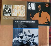 Three vinyl albums on a red patterned surface showing Lightning Hopkins Early Recordings, Son House 1941-42 Recordings, and Kings of Country Blues Vol. 2 with photos of multiple artists.