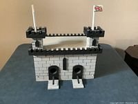 Front view of the handmade bird house depicting two entry holes with perches, battlement details, and flagpole with flag on top of right tower.