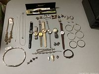 Photo of entire lot spread out on table showing watches, cuff links, necklaces, bracelets, earrings, pendants, and ring.
