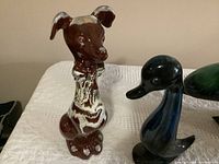 Photo showing brown dog and blue duck Blue Mountain Pottery figurines on white surface.