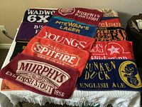 Fourteen colorful British bar towels featuring beer branding and logos, laid out on a surface.