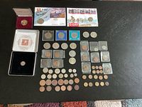 Full assortment of coins displayed on a dark surface including several coins in protective holders and cases, various sizes from pennies to larger coins.