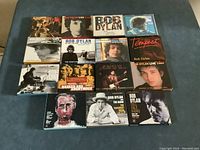 Top down view of 15 Bob Dylan double CD jewel cases arranged on blue surface, showing album artwork on the front covers.