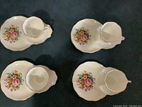 Four sets of bone china tea cups and matching divided biscuit plates with floral rose patterns, displayed from a top angle