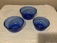 Set of three blue glass mixing bowls in different sizes on a beige cloth background.
