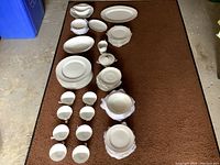 Full view of nearly all the dishes laid out, showing white porcelain set with floral embossed rims and various sized plates, bowls, cups, and serving pieces visible.