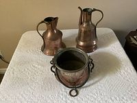 Photo showing three vintage solid copper pieces: one pot and two jugs, front view