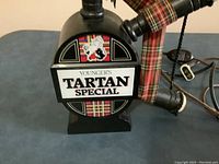 Front view of bagpipe shaped lamp with Youngers Tartan Special logo, showing tartan fabric details and lamp base.