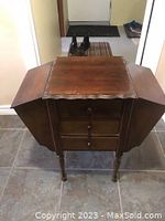 Full view of vintage Martha Washington sewing cabinet with flip top sides extended, showing dark wood with scalloped edges.