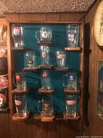 Front view of wooden display shelf holding 12 British beer glasses and mugs with various brand logos.
