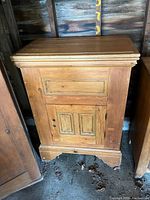 Front view of antique wooden refrigerator showing hinged top, locked bottom door, and natural wood finish.