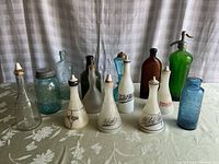Photo showing a collection of antique and vintage glass bottles including milk glass condiment bottles, a blue Mason jar, and vintage colored glass bottles.