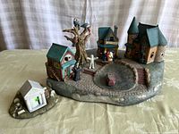 Overview of ceramic Halloween village on base, showing layout of buildings, figures, tree, and graveyard.