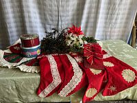 Photo showing four red vintage Christmas stockings with lace and snowflake patterns, quilted tree skirt beneath, two round cookie tins with holiday designs, and two faux poinsettia flower arrangements (red and white).