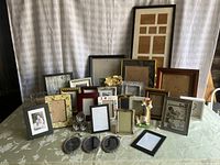 Wide view showing multiple metal and wood picture frames arranged on table, sizes vary from small to large.