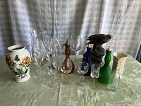 Wide view of all items on table showing ceramic vase, etched glassware, vintage bottles, and ceramic eagle.