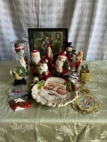 Wide view showing entire collection on table with various Santa figurines, plate, ornaments, and snow globe.