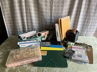 Photo showing a variety of office supplies including Mead notebooks, folders, sticky tabs, envelopes, pencils, hole puncher, and tape dispenser arranged on a table.