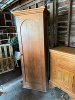 Full view of vintage wooden cabinet showing its tall single door with an arched panel design and aged wood finish.
