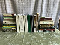 Full view of the 29 environmental and urban planning books arranged in three groups stacked on bedding, showing varied sizes and colors.