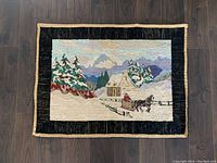 Full view of the antique hooked rug laid flat on a wooden floor, showing the complete winter scene and border.