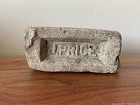 Front-facing photo of the rectangular brick showing the embossed text 'J. PRICE' on one side, placed on a wooden surface against a plain white wall.