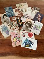 Photo showing the overall lot of vintage and antique postcards, cigarette cards, and playing card arranged on a wooden surface.