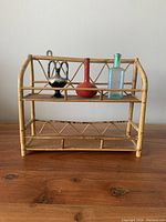 Front view of vintage bamboo shelf with two small bud vases and one antique glass bottle displayed on the middle tier.