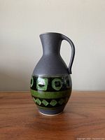Side view of vintage West Germany ceramic pitcher with matte dark gray finish and green geometric patterned band.