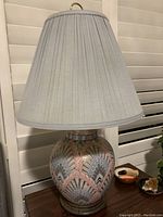 Full lamp showing pleated soft blue lampshade on ceramic base with art deco design and wooden base