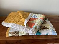 Folded view of vintage patchwork quilt showing mustard yellow backing and colorful geometric patchwork front.
