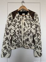Full front view of Wilfred Aritzia jacket hung on wooden hanger, showing pattern and brown leather patch details on shoulders, zippered pockets, and zip front closure.