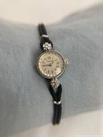 Full view of watch showing gold case, diamonds at 12/6 o'clock, silver dial and black silk strap.