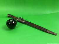 Photo of full bayonet with scabbard laid diagonally on green background