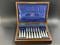 Open wooden box with blue silk interior displaying mother-of-pearl-handled knives and forks