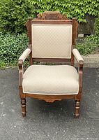 Front view of the walnut Eastlake armchair showing carved crest rail, upholstered backrest and seat, and turned legs.
