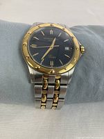 Front view of watch on cushion showing black dial, gold-tone bezel and two-tone bracelet