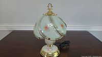Full view of lamp showing scalloped glass shade with painted flowers and brass-tone metal base