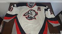 Full photo of white CCM hockey jersey with sabres logo, number 10 and letter 'A' on front.