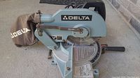 Front side of the Delta mitre saw showing the saw blade, dust collection bag, and overall structure.