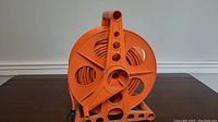 Front-side view of orange extension cord reel showing multiple circular cutouts and orange cord wound around it