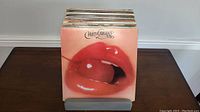Vinyl records stacked in grey plastic holder on wooden table, showing front cover of Wild Cherry album with close-up of lips and cherry.