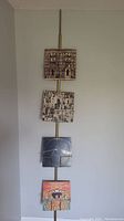 Full view of the spring-loaded vertical record holder mounted from floor to ceiling holding 4 vinyl LP records.
